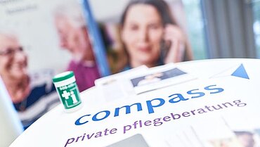 Nahaufnahme eines Stehtischs mit Infomaterial und Notfalldose von compass private pflegeberatung.