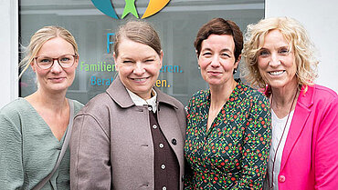 Vier Frauen stehen lachend vor einem Fenster, auf dem das FIBS-Logo klebt.