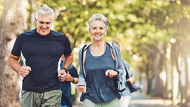 Zwei Menschen mittleren Alters, ein Mann und eine Frau, joggen auf einer Allee.