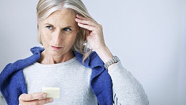 Eine Frau hat einen Notizzettelblock in der einen Hand und fasst sich mit der anderen Hand an die Schläfe.