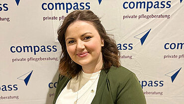 Porträt von Aida Muratovic vor einer Fotowand mit compass-Logos.