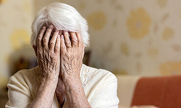 Eine alte Frau vergräbt ihr Gesicht in ihren Händen.