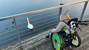 Ein Kind im Rollstuhl beobachtet einen schwimmenden Schwan.