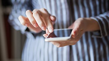 Nahaufnahme von zwei Händen, die ein Smartphone in der Hand halten und auf den Bildschirm tippen.